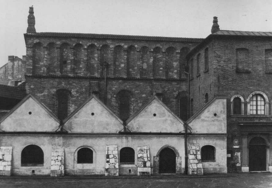 Photographie en noir et blanc d'un grand bâtiment en briques avec plusieurs toits pointus à pignon, identifié comme une synagogue historique.