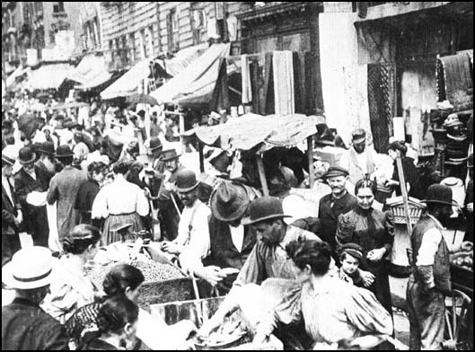 Old photograph of a bustling market street on New York's Lower East Side, stalls and a crowd of passers-by.