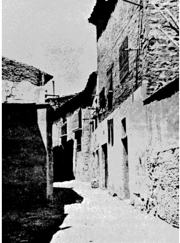 Black-and-white photograph of a cobbled alley in the old Jewish quarter of Tudela, Spain — stone façades and a central well.