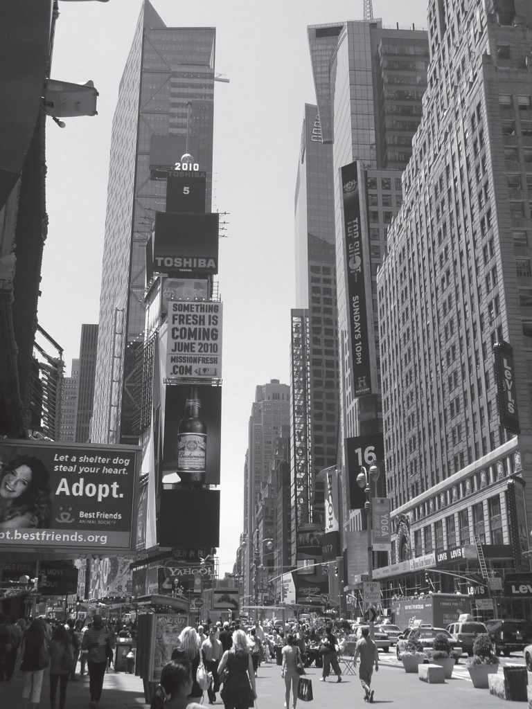 Photographie en noir et blanc de Times Square à New York, avec ses nombreux panneaux publicitaires et enseignes lumineuses (Toshiba, etc.) dominant la foule.