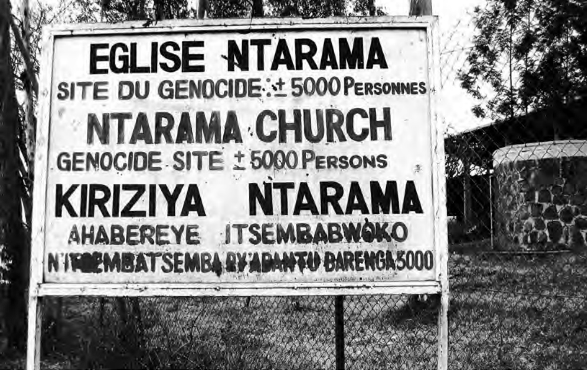 A large signboard at the entrance of the site, bearing the inscription 'NTARAMA CHURCH GENOCIDE SITE ± 5000 PEOPLE' in French, English and Kinyarwanda.