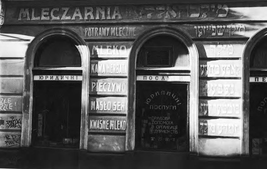 Photograph of a wooden dairy storefront with numerous signs and inscriptions in Polish and Ukrainian.
