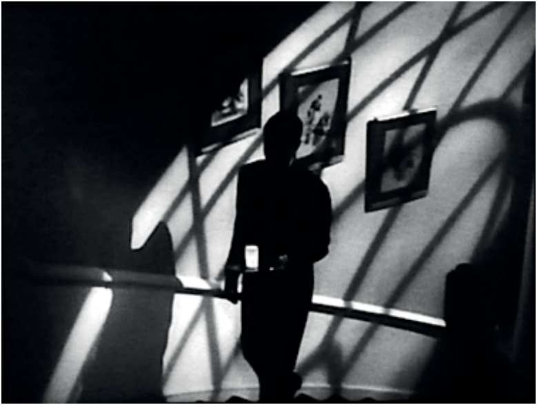 Black-and-white film still: Cary Grant in a dark suit, climbing a staircase while carrying a luminous glass of milk, in *Suspicion*.